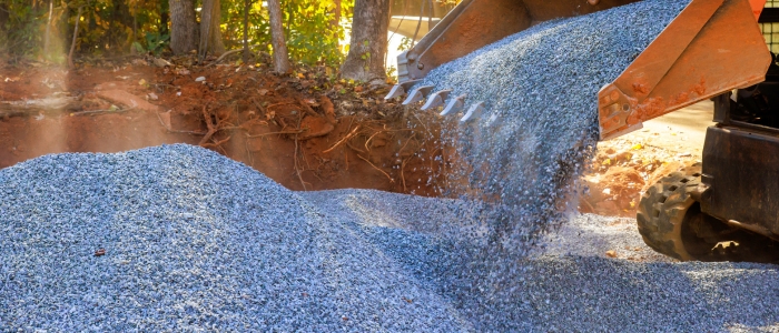 A dump truck unloading gravel to create a pile for chip seal driveway resurfacing with crushed stone.