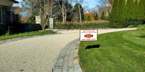A gravel driveway in Old Saybrook, CT, featuring a New England Asphalt sign, marked as a single chip seal surface.