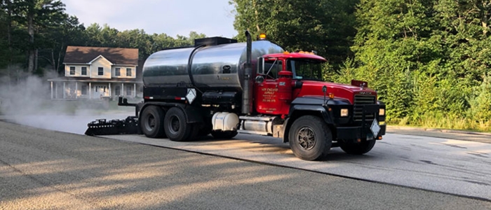 A truck applying hot liquid to a road surface as part of the chip seal paving process, illustrating binder application.