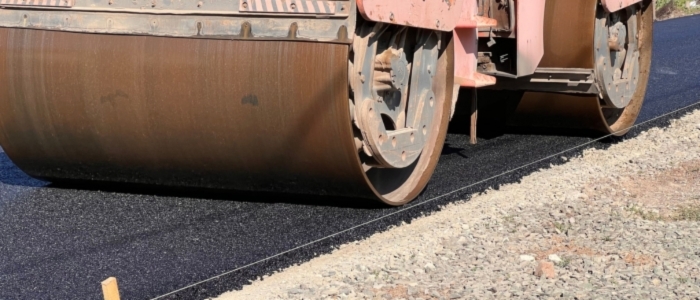 A roller compacts asphalt on a road, demonstrating the process of chip seal paving and ensuring a smooth surface.