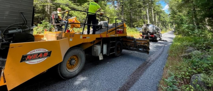A man is actively working on road with a truck for surface preparation for chip seal paving.