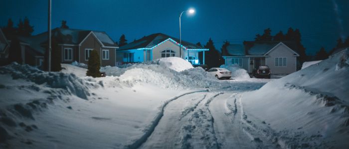 A snowy street at night, with a chip seal surface reflecting the soft glow of streetlights.