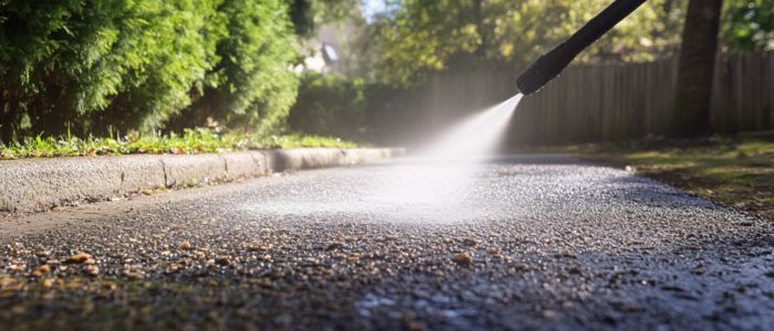 Close-up of a pressure washer cleaning a chip seal driveway.
