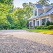 Light-colored chip seal driveway curving through a landscaped front yard toward a traditional house.