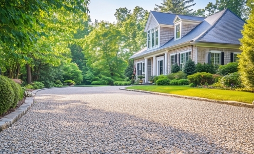 Light-colored chip seal driveway curving through a landscaped front yard toward a traditional house.