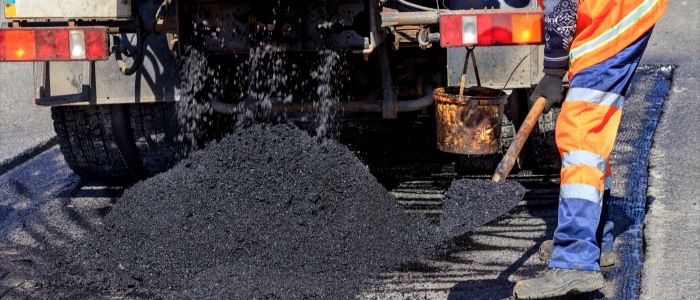 A man pours asphalt onto a road, demonstrating the process of asphalt paving in a construction setting.