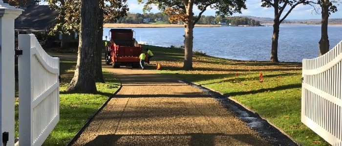 A pathway leading to a lake, with a tractor and boat visible, representing chip seal versus asphalt maintenance and repairs.