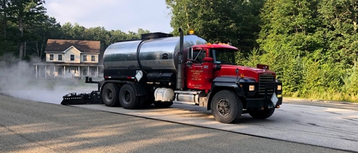 A large truck working on a road, illustrating a process related to chip seal driveway installation.