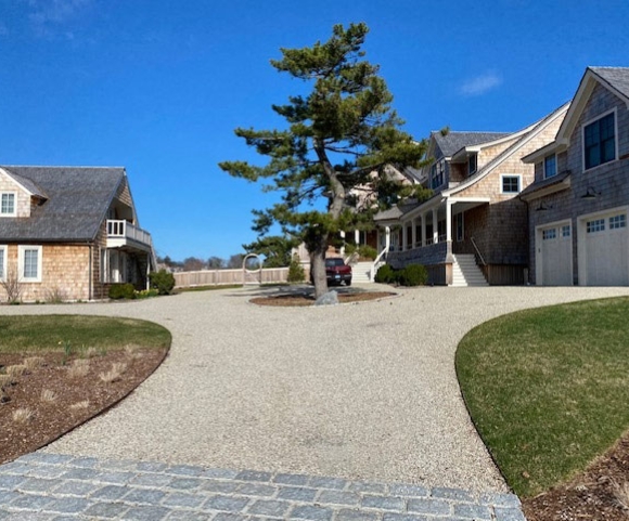 An oil and stone driveway in Connecticut, showcasing two garages and a tree alongside the path.