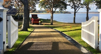 A driveway leading to a lake, with a parked tractor in front, showcasing a low-maintenance oil and stone surface.