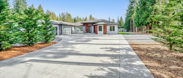A concrete driveway with trees leading to a garage, illustrating a durable and long-lasting driveway option.