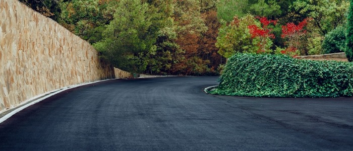 A view of a road bordered by a wall and trees, representing durable asphalt driveways in a natural setting.