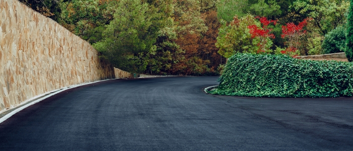 A view of a road bordered by a wall and trees, representing durable asphalt driveways in a natural setting.