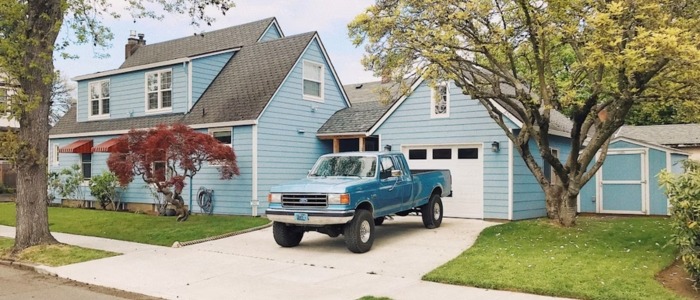 A blue house with a pickup truck parked outside, showcasing a concrete driveway known for its durability.