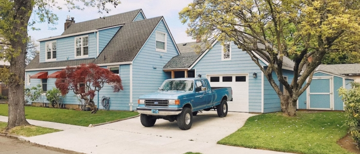 A blue house with a pickup truck parked outside, showcasing a concrete driveway known for its durability.