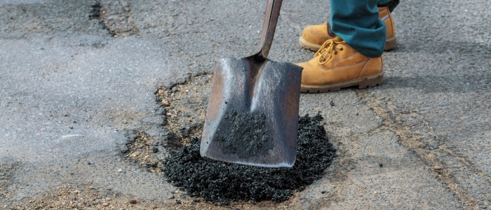 A person shovels asphalt, demonstrating maintenance techniques for long-lasting driveways through crack filling and patching.