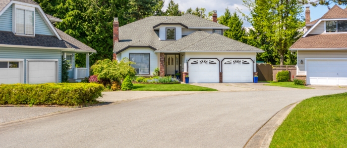 A residential driveway with two garages adjacent to a house, featuring a concrete finish.