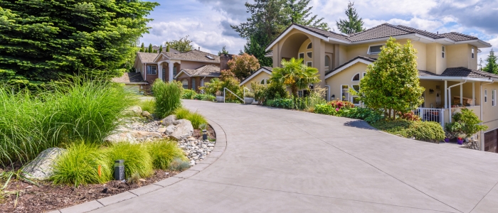 A home driveway with landscaped surroundings, highlighting considerations for chip seal and concrete maintenance choices.