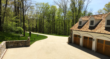 A driveway leading to a garage with a wood shingled roof, showcasing the aesthetic appeal of an oil and stone finish.
