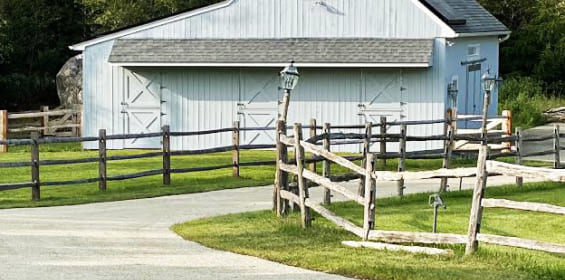 A barn with a surrounding fence and a well-maintained oil and stone driveway in Madison, CT.