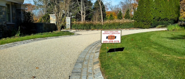 A gravel driveway displaying a sign of New England Asphalt related to selecting the appropriate contractor for oil and stone rejuvenation services.