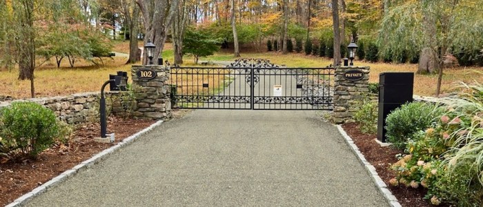 A gated driveway with a stone walkway, representing the concept of rejuvenating versus replacing driveways.