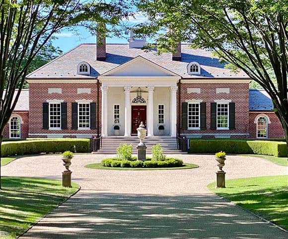 A grand brick estate with a white columned portico and a circular gravel driveway.
