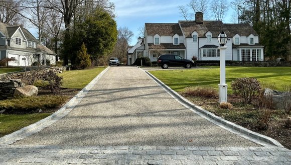 A driveway featuring a stone path that leads directly to a house surrounded by greenery.