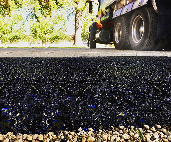 Close-up of fresh, dark asphalt being applied to a driveway with a truck in the background.