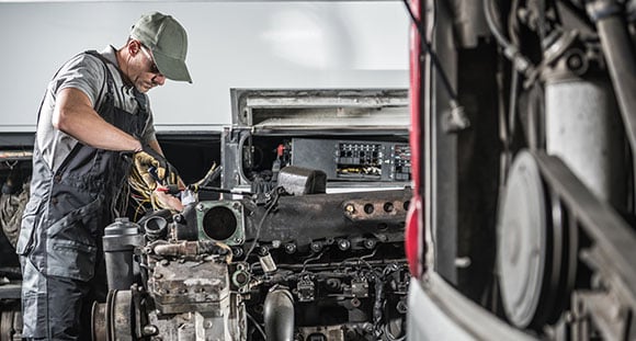 Mechanic in a baseball cap and overalls working on a large diesel engine.